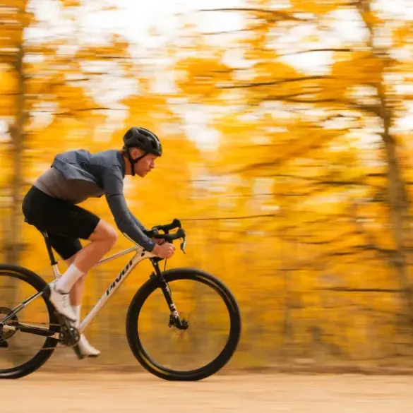 Ein Mann in voller Fahrt auf einem weißen Mountainbike mit Rennlenker, umgeben von verschwommenen gelben Herbstblättern.