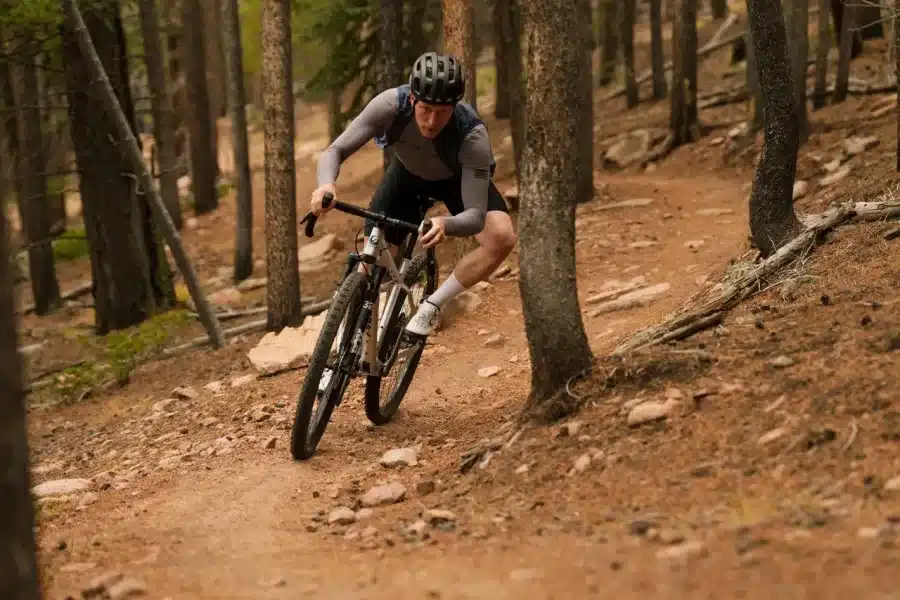 Ein Radfahrer auf einem silbernen Mountainbike mit Rennlenker fährt auf einem steinigen Waldweg.