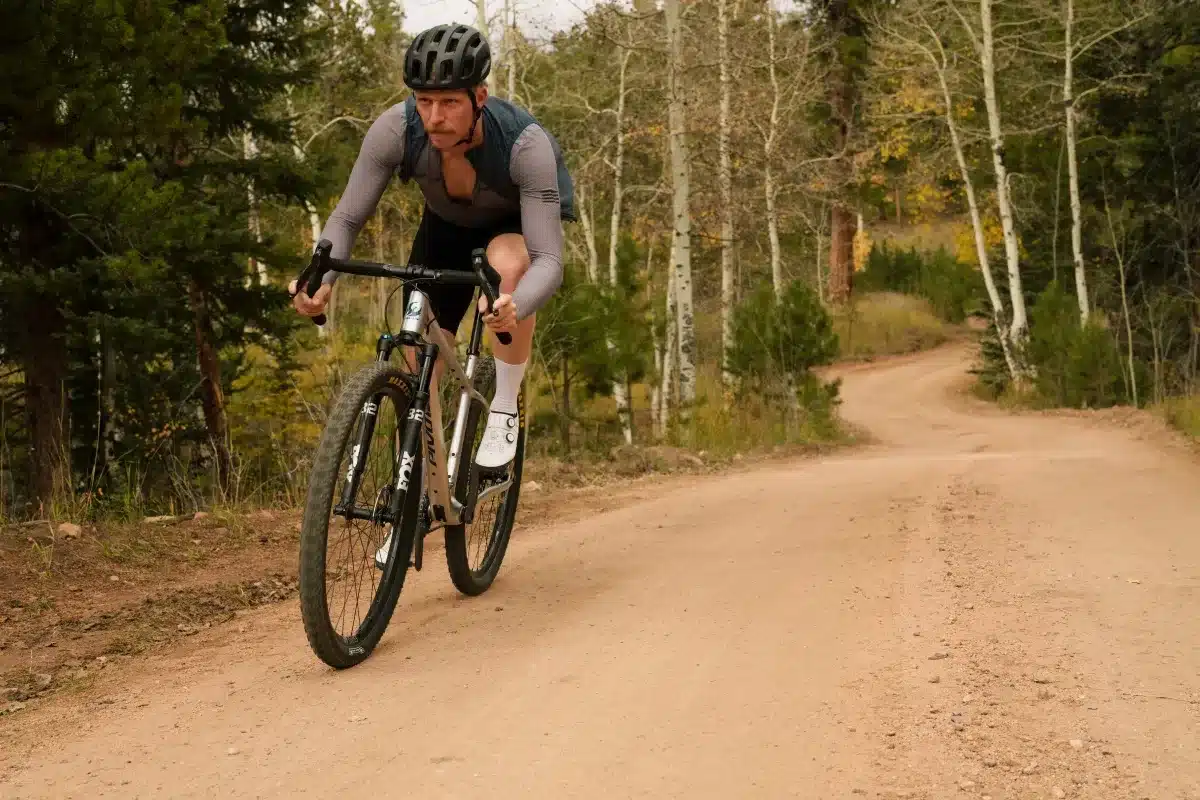 Ein Mann fährt auf einem Pivot LES SL Drop Bar Mountainbike auf einer staubigen Schotterstraße durch einen Wald.