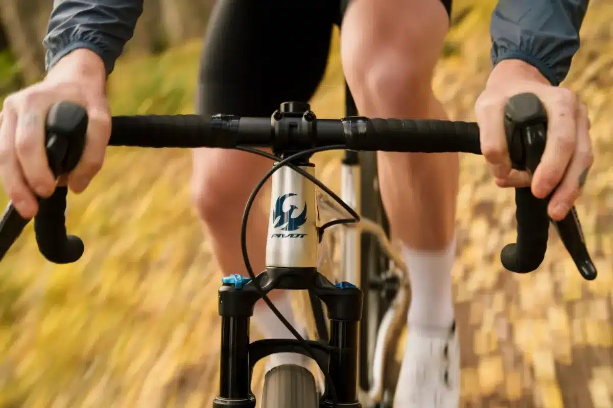 Nahaufnahme des Dropbar-Lenkers mit Bremshebeln und dem Pivot-Logo auf dem Steuerrohr, während eine Person das Fahrrad fährt.