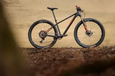 Ein schwarzes Pivot Les SL Cross-Country-Hardtail steht auf erdigen Blättern, das Vorderrad zeigt eine goldene Federgabel.