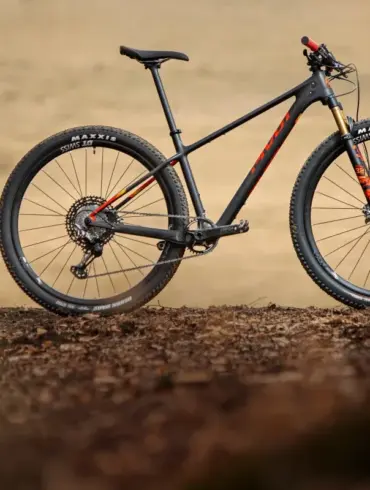Ein schwarzes Pivot Les SL Cross-Country-Hardtail steht auf erdigen Blättern, das Vorderrad zeigt eine goldene Federgabel.