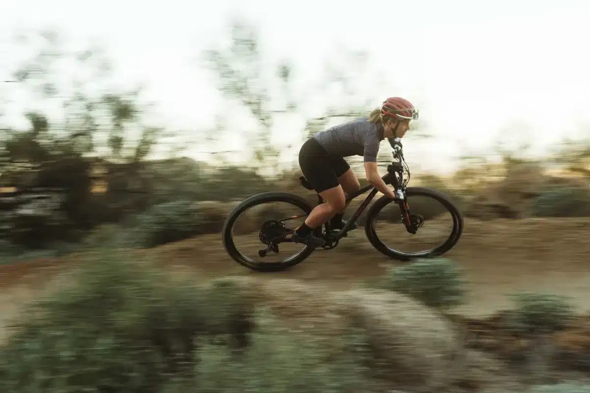 Frau mit Helm und sportlicher Kleidung fährt mit einem Pivot Les SL Mountainbike auf einem staubigen Trail im Gelände.