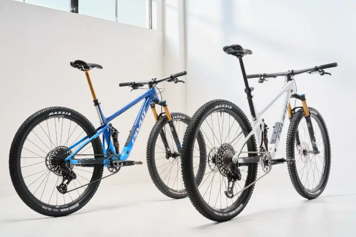 Zwei Vollcross-Country-Mountainbikes von Pivot Cycles, ein blaues und ein weißes, stehen nebeneinander in einem Studio.