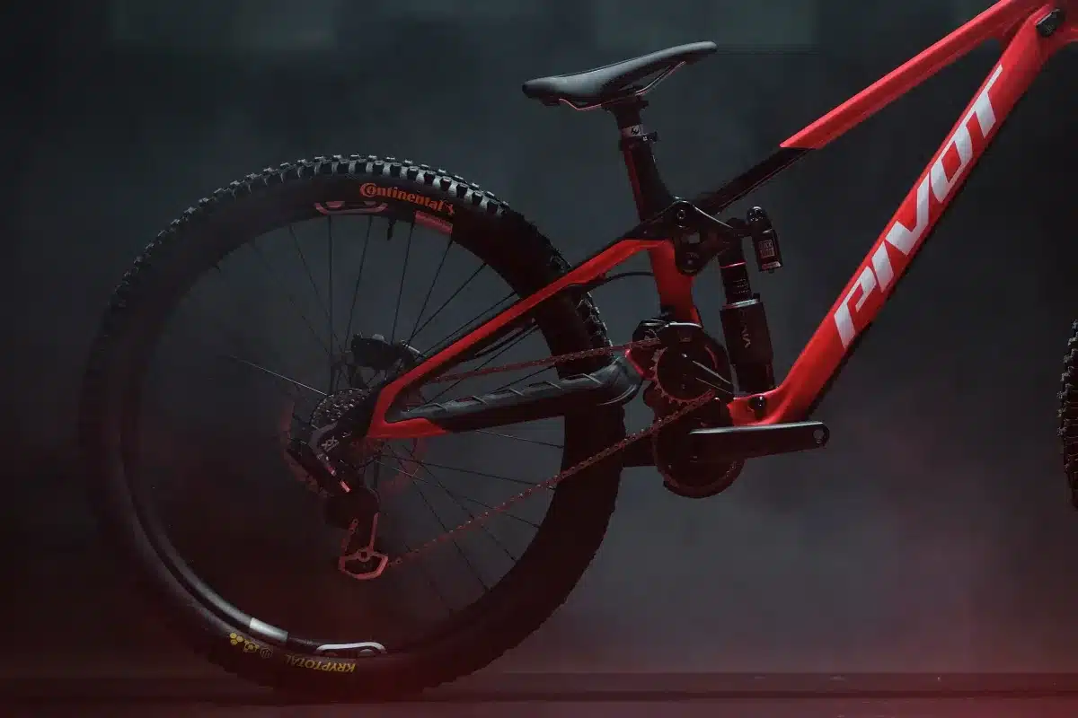 Detailaufnahme des Hinterbaus und des Antriebsstrangs eines roten Pivot Phoenix Downhill-Mountainbikes im Studio, mit Nebel im Hintergrund.