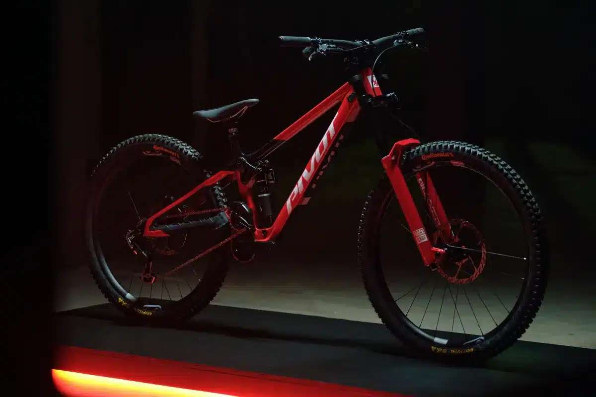 Rotes Pivot Phoenix Downhill-Mountainbike mit schwarzen Akzenten und RockShox Gabel, im dunklen Studio mit rotem Lichteffekt.