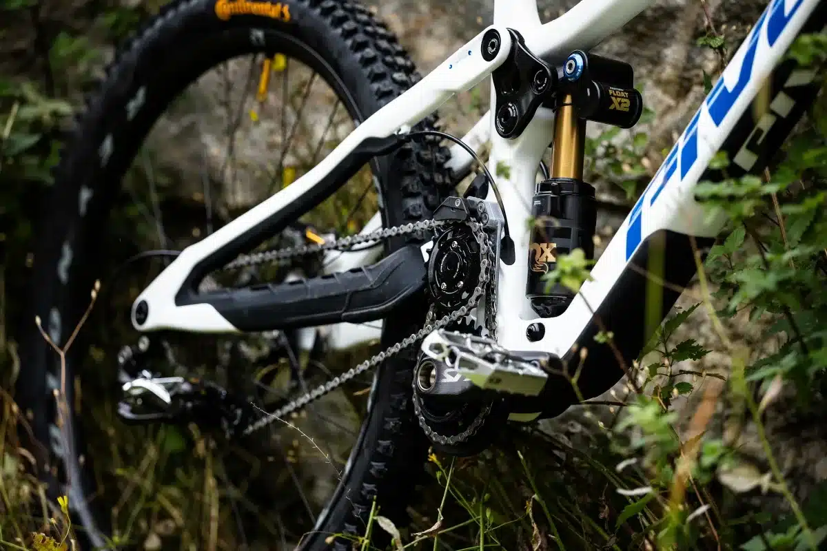 Detailaufnahme des Hinterbaus eines weißen Pivot Phoenix Downhill-Mountainbikes, Fokus auf Dämpfer, Kettensystem und Reifen.
