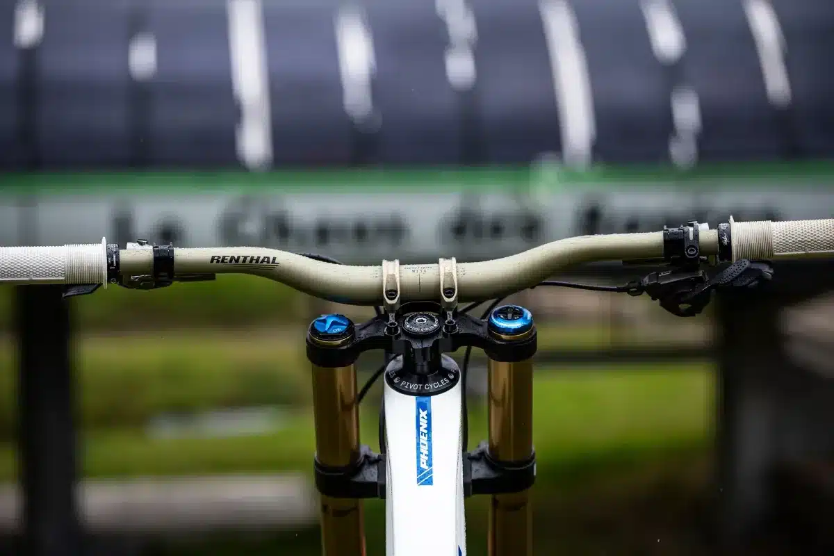 Nahaufnahme des Lenkers und der Gabelbrücke eines weißen Pivot Phoenix Downhill-Bikes mit goldenen Federelementen.