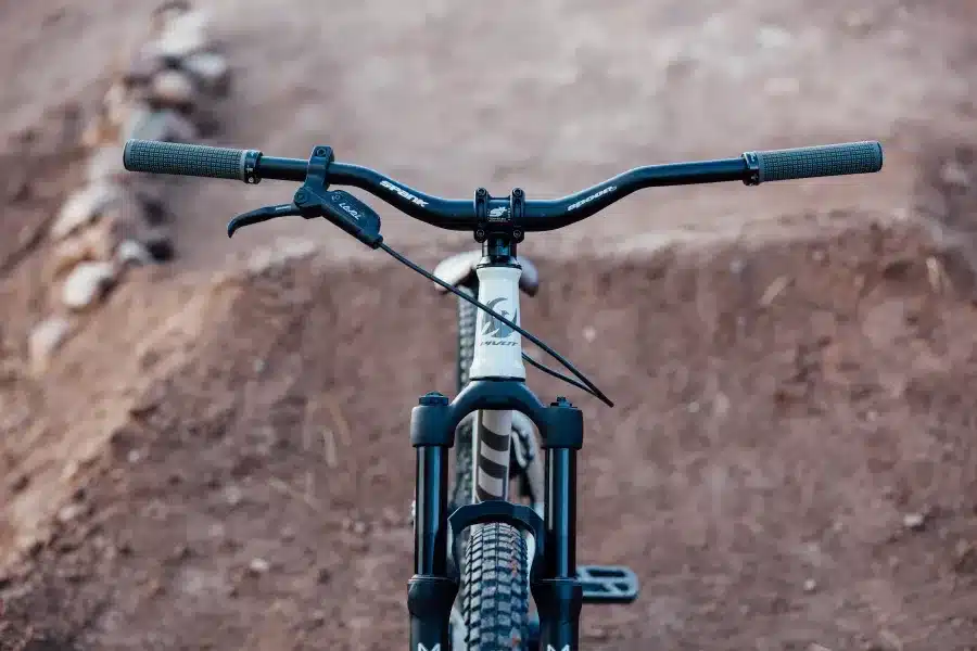 Vorderansicht eines weißen Pivot Point Dirtjump-Bikes mit schwarzem Lenker und Federgabel, aufgestellt auf einem Erdhügel.