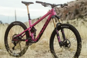 Ein pinkfarbenes Pivot Shadowcat Mountainbike mit 27,5-Zoll-Laufrädern, Fox-Federung und Maxxis-Reifen, das auf einem staubigen Untergrund steht.