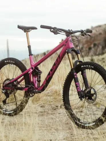 Ein pinkfarbenes Pivot Shadowcat Mountainbike mit 27,5-Zoll-Laufrädern, Fox-Federung und Maxxis-Reifen, das auf einem staubigen Untergrund steht.