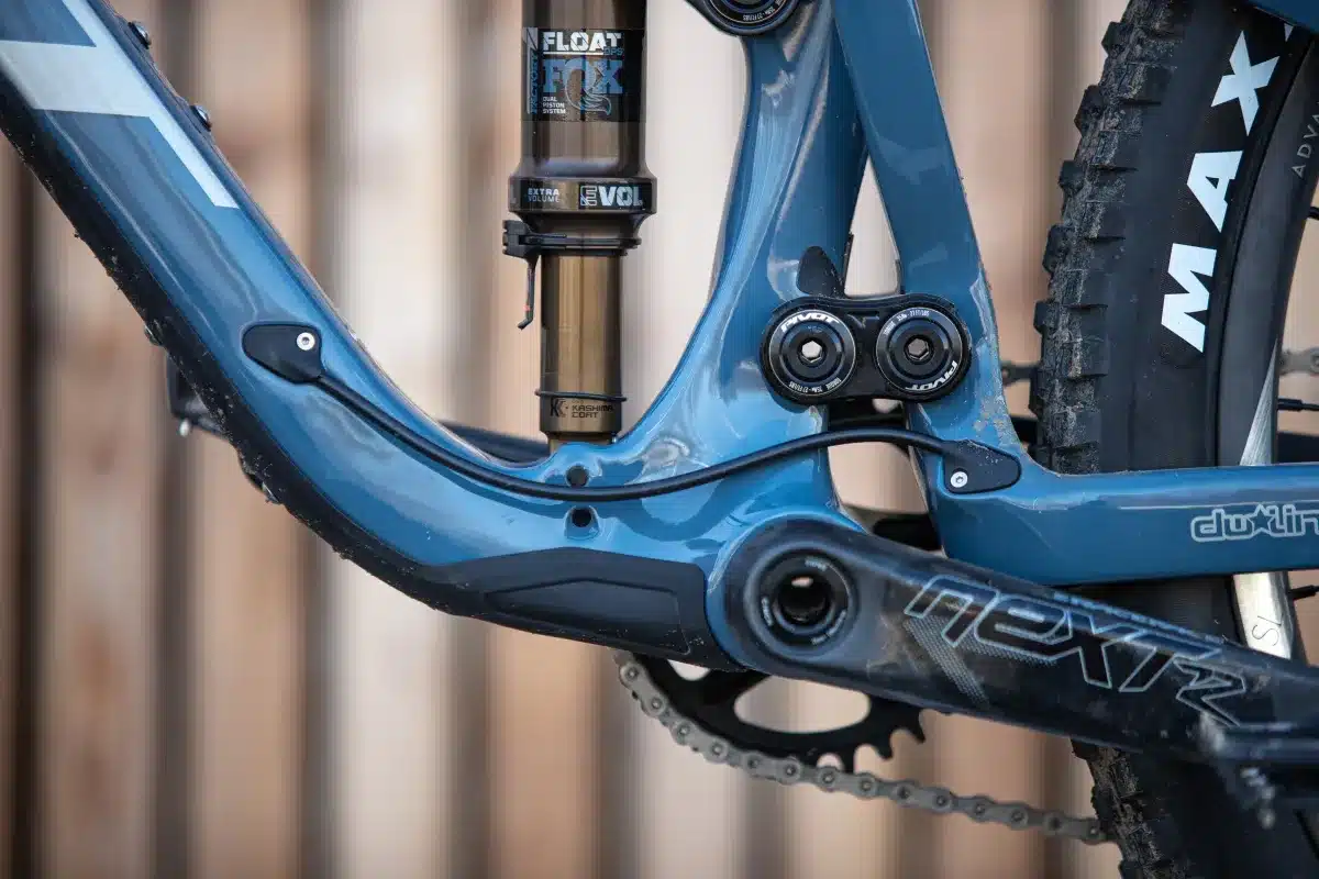 Nahaufnahme des blauen Vollfederungsrahmens eines Pivot Shadowcat Mountainbikes. Man sieht den Fox Float DPS Kashima Coat Dämpfer, die dw-link-Kinematik und die Race Face Next Kurbel. Im Hintergrund ist ein Maxxis Reifen zu erkennen.