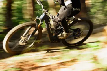 Ein Fahrer auf einem Pivot Shuttle AM E-Mountainbike fährt durch einen Waldweg, die Räder und der Hintergrund sind durch die Bewegung unscharf.