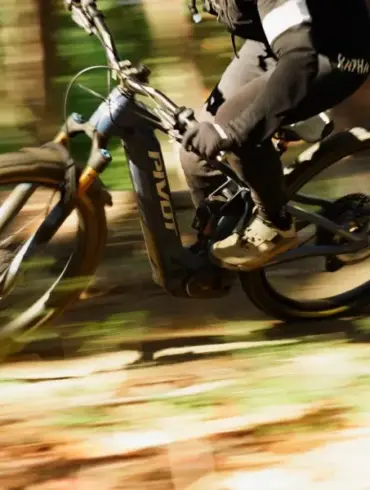Ein Fahrer auf einem Pivot Shuttle AM E-Mountainbike fährt durch einen Waldweg, die Räder und der Hintergrund sind durch die Bewegung unscharf.