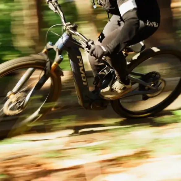 Ein Fahrer auf einem Pivot Shuttle AM E-Mountainbike fährt durch einen Waldweg, die Räder und der Hintergrund sind durch die Bewegung unscharf.