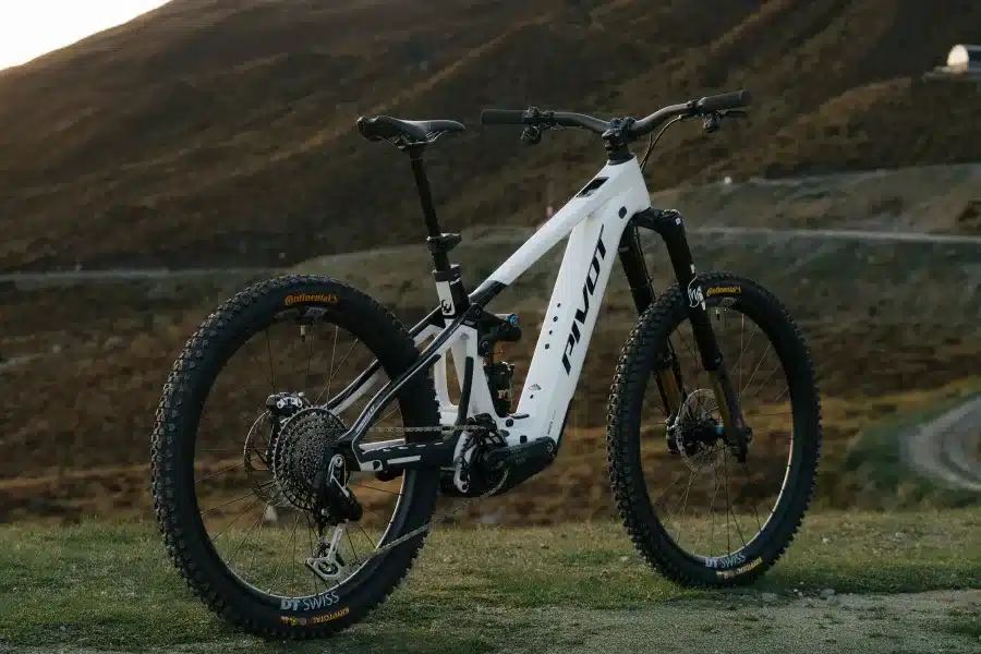 Ein weißes Pivot Shuttle LT Elektro-Enduro Mountainbike steht seitlich auf einem Hügel, bereit für anspruchsvolles Gelände. Das Fahrrad ist mit breiten Reifen, Federung und einem Bosch-Antrieb ausgestattet.