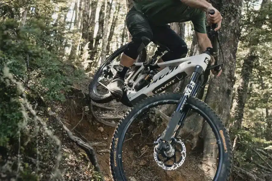 Fahrer auf einem weißen Pivot Shuttle LT E-Mountainbike fährt bergab auf einem steilen, wurzeligen Waldweg.