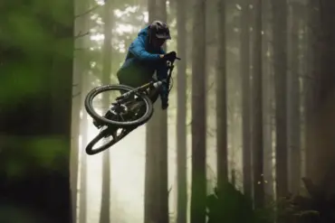 Mountainbiker im Sprung in einem Wald mit Bäumen und Nebel im Hintergrund