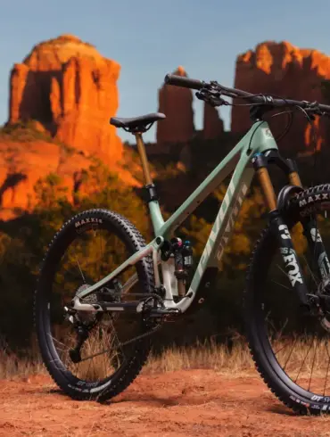 Ein hellgrünes Pivot Trailcat LT Mountainbike steht auf einem roten, staubigen Untergrund vor einer Felsformation im Abendlicht.