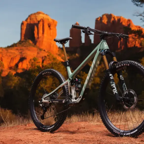 Ein hellgrünes Pivot Trailcat LT Mountainbike steht auf einem roten, staubigen Untergrund vor einer Felsformation im Abendlicht.