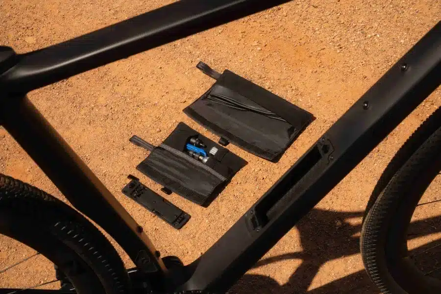 Nahaufnahme des schwarzen Rahmens eines Pivot Vault Gravelbikes, das ein integriertes Staufach zeigt, aus dem eine offene schwarze Werkzeugtasche mit Werkzeugen und eine zusätzliche schwarze Tasche herausragen.