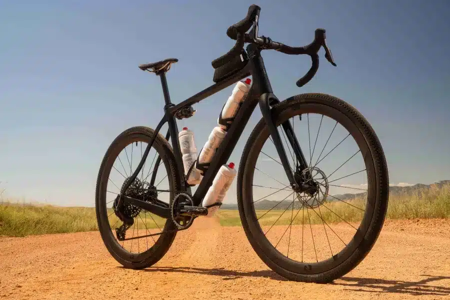 Ein schwarzes Pivot Vault Gravelbike steht auf einem Feldweg mit trockener Vegetation und Bergen im Hintergrund.