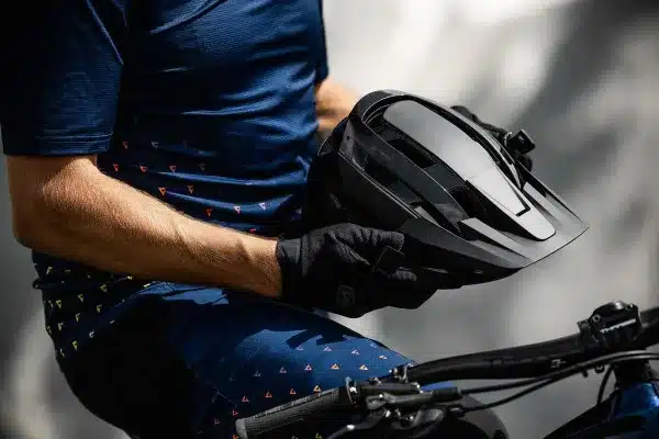 Ein Mann mit Handschuhen hält einen schwarzen MTB-Helm mit Visier.