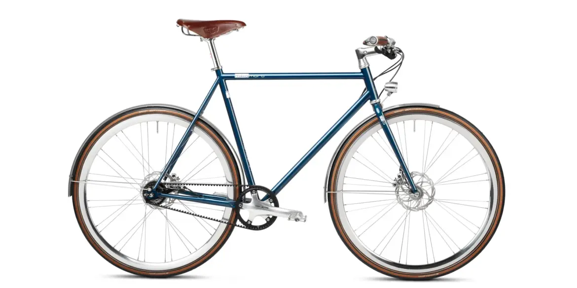 Seitenansicht des Solid Petrol Urban Deluxe Bikes, einem dunkelblauen Fahrrad mit braunem Ledersattel, Riemenantrieb und integrierter Lichtanlage.