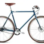 Seitenansicht des Solid Petrol Urban Deluxe Bikes, einem dunkelblauen Fahrrad mit braunem Ledersattel, Riemenantrieb und integrierter Lichtanlage.