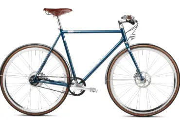 Seitenansicht des Solid Petrol Urban Deluxe Bikes, einem dunkelblauen Fahrrad mit braunem Ledersattel, Riemenantrieb und integrierter Lichtanlage.