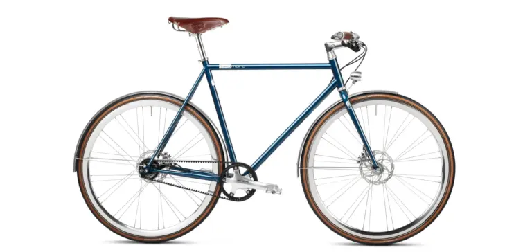 Seitenansicht des Solid Petrol Urban Deluxe Bikes, einem dunkelblauen Fahrrad mit braunem Ledersattel, Riemenantrieb und integrierter Lichtanlage.