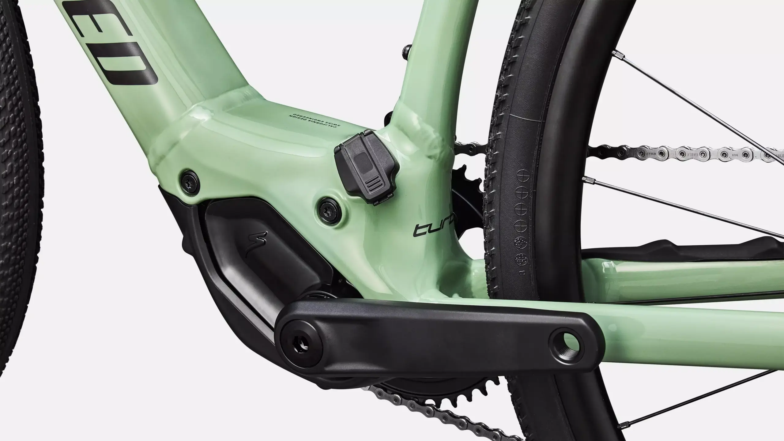 Detailansicht des Specialized Turbo Creo 2 Comp E5 E-Gravelbikes. Man sieht das hellgrüne Aluminiumrahmen-Detail mit dem Schriftzug 'Turbo', die Kurbelgarnitur, die Kette und das Hinterrad mit Reifen.