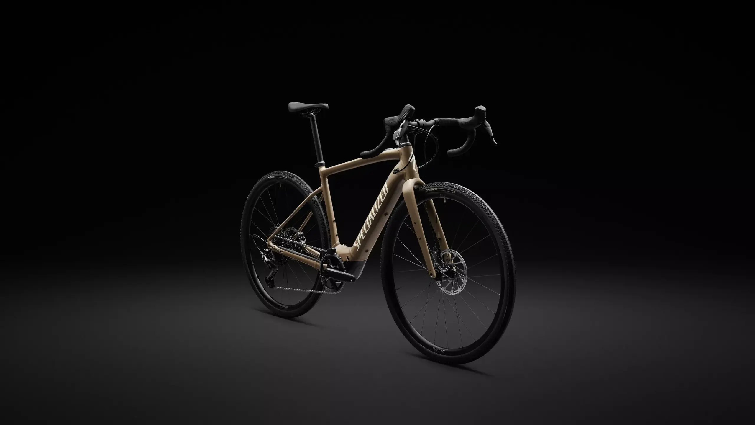 Ein sandfarbenes Specialized Turbo Creo 2 Comp E5 E-Rennrad mit Rennlenker und breiten Reifen steht vor einem dunklen Hintergrund.
