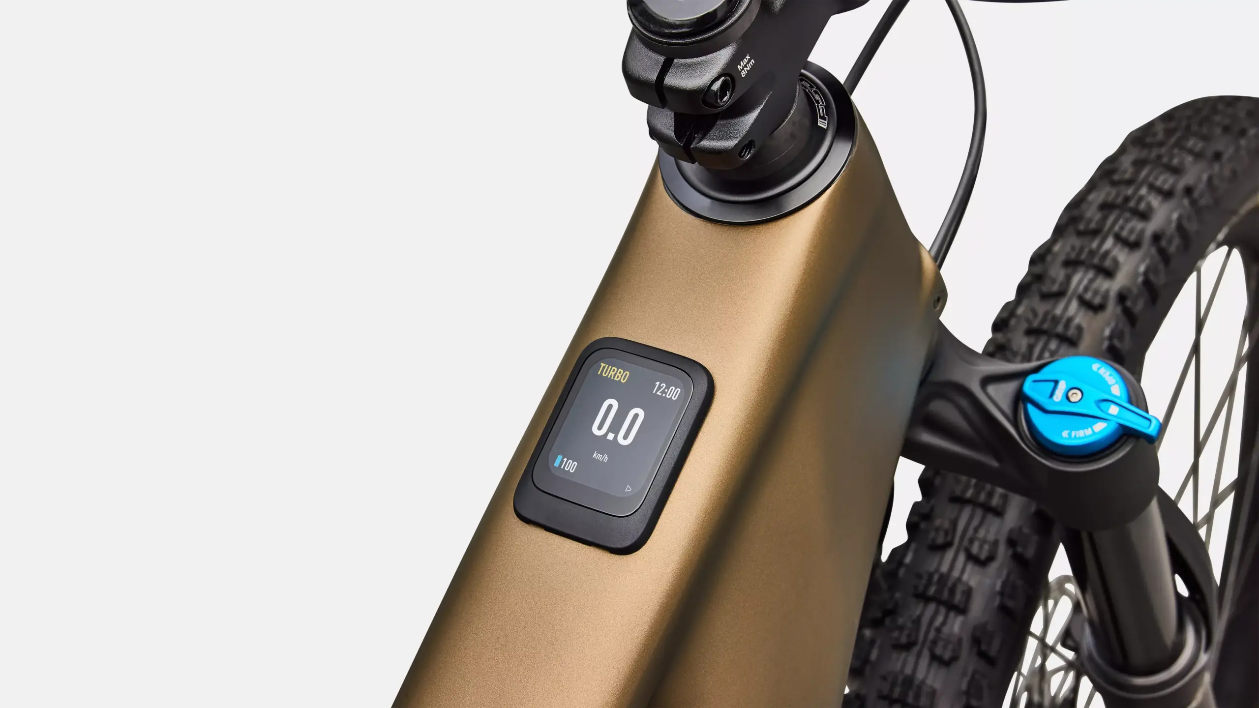 Detailaufnahme des bronzefarbenen Rahmens eines Specialized Turbo Levo R Comp E-Mountainbikes mit einem integrierten Display, das Geschwindigkeit und Akkuladung anzeigt, sowie der vorderen FOX Federgabel.