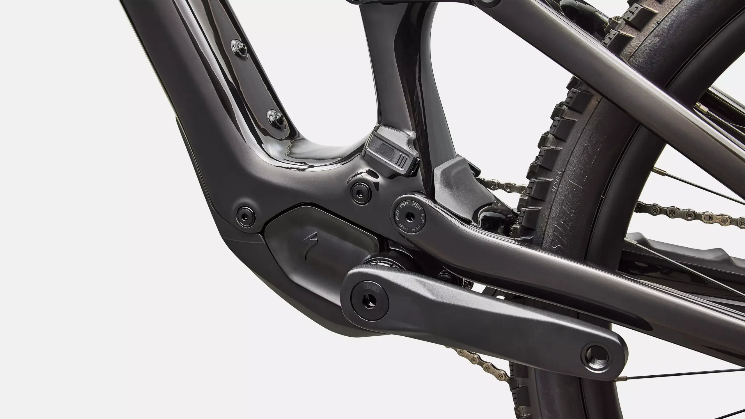 Nahaufnahme des dunklen Carbon-Rahmens eines Specialized Turbo Levo SL 2 Expert Di2 E-Mountainbikes, die den Bereich des integrierten Motors, die Kurbel und Teile des Hinterrads mit Kette zeigt.