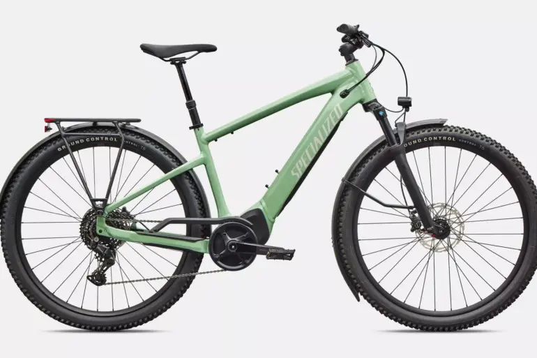 Ein pistaziengrünes Specialized Turbo Tero 4.0 EQ E-Bike mit Gepäckträger, Schutzblechen und integriertem Akku, freigestellt vor weißem Hintergrund.