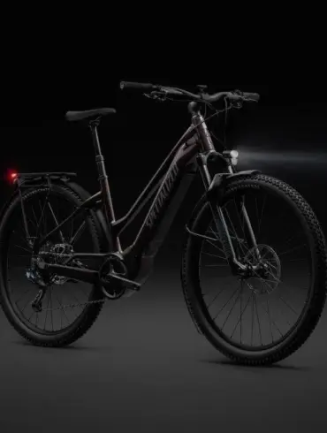 Dunkelrotes Specialized Turbo Tero 5.0 EQ E-Bike mit schwarzem Gepäckträger, Schutzblechen, Vorder- und Rücklicht auf dunklem Hintergrund.