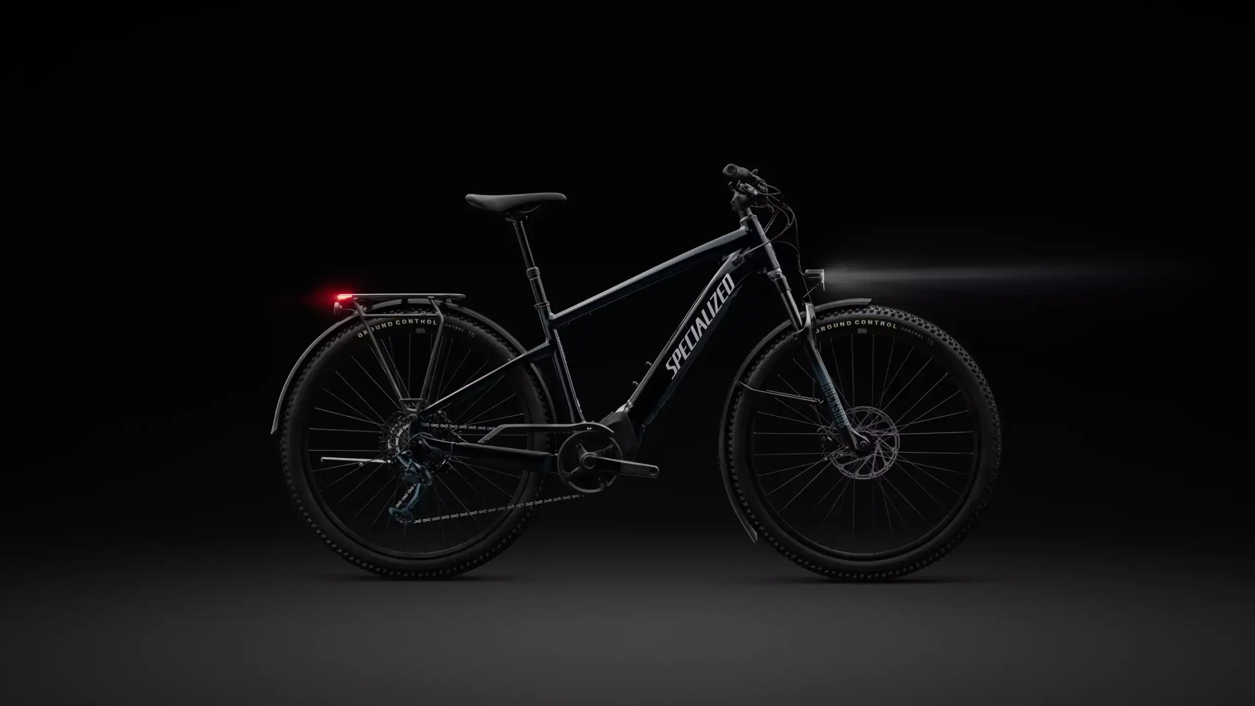 Studioaufnahme eines schwarzen Specialized Turbo Tero 5.0 EQ E-Bikes mit Beleuchtung und Gepäckträger auf schwarzem Hintergrund.