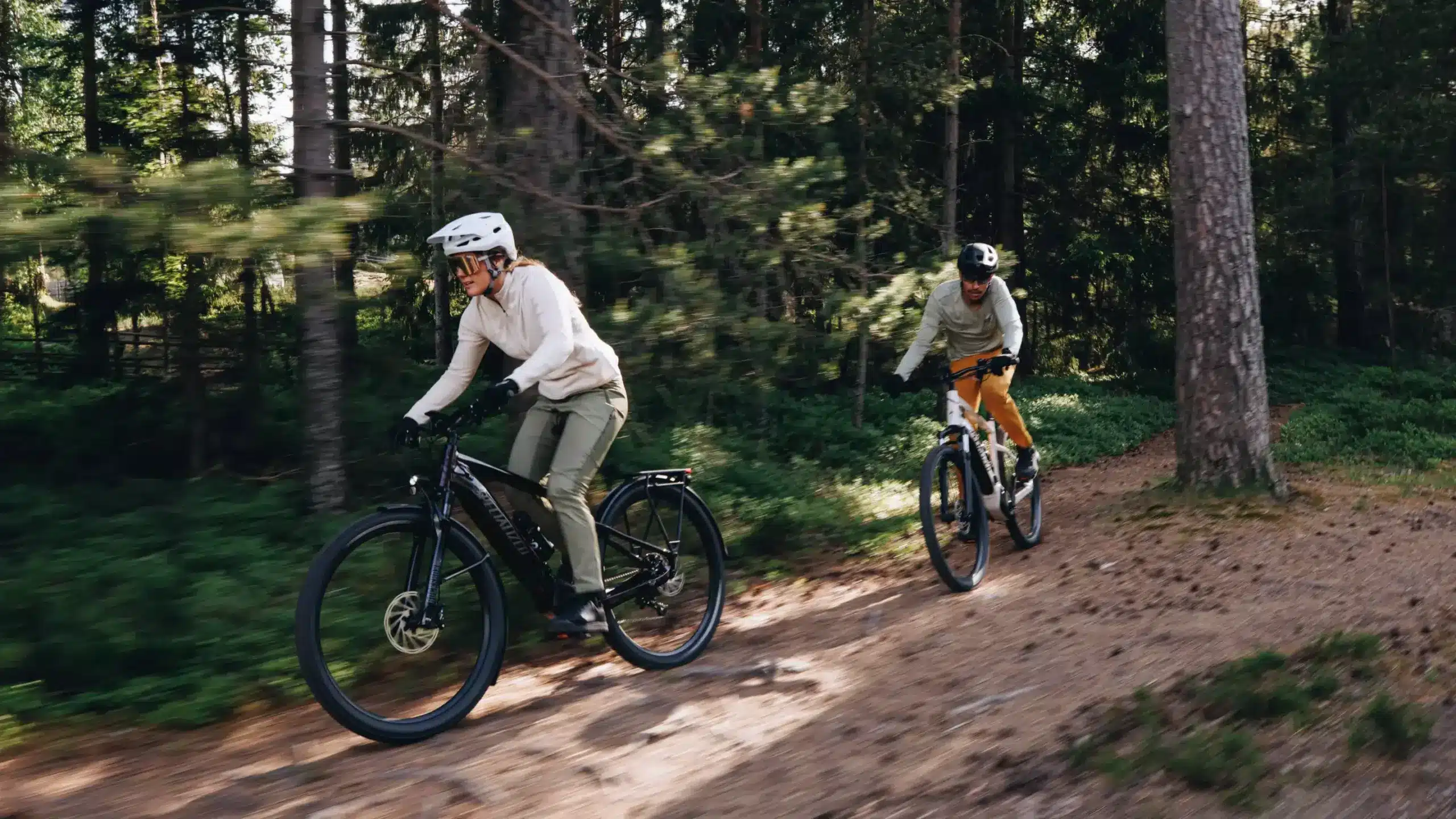 Zwei Radfahrer mit Helm und Fahrradbrillen fahren auf einem dirtigen Waldweg mit ihren Specialized Turbo Tero 5.0 EQ E-Bikes. Eine Person fährt vor der anderen.