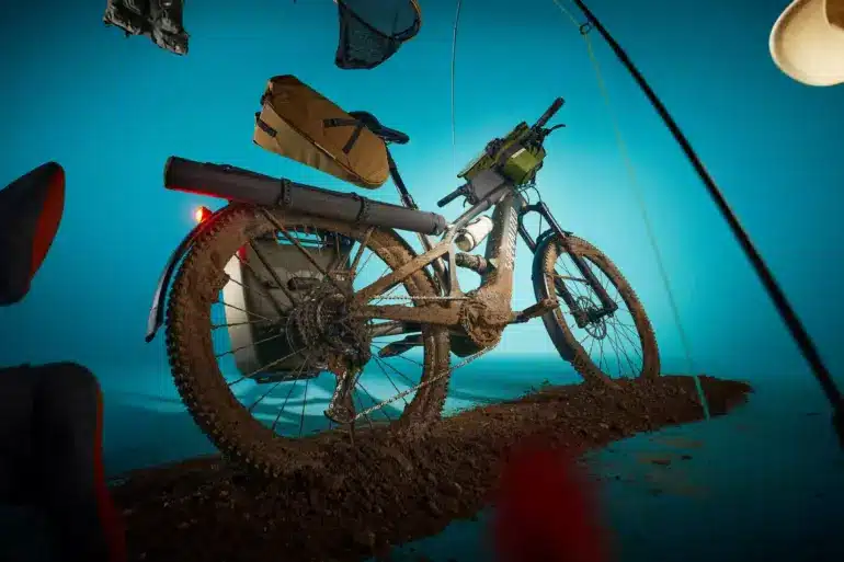 Specialized Turbo Tero X 4.0 E-Bike mit voller Ausstattung und im Schlamm liegend, dargestellt mit einem blauen Hintergrund und umgebenden Gegenständen wie Angelrute und Hut.
