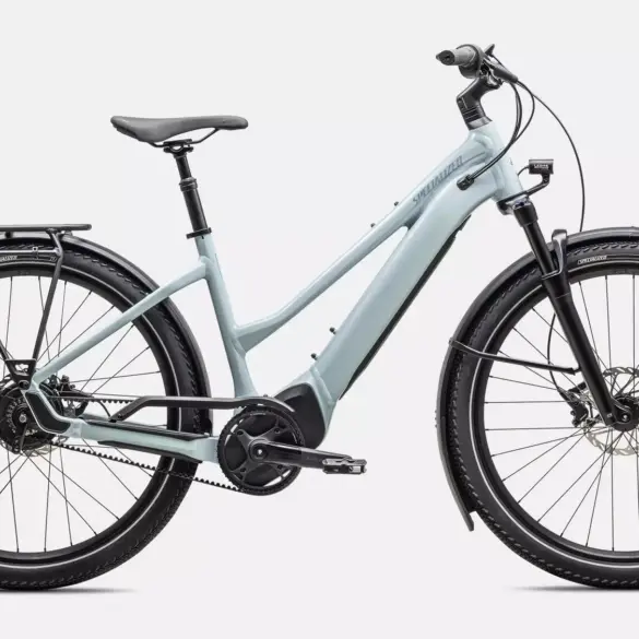 Das Specialized Turbo Vado 4.0 IGH Step-Through ist ein hellgraues E-Bike mit tiefem Einstieg. Es verfügt über Schutzbleche, einen Gepäckträger, eine integrierte Beleuchtung und breite Reifen. Der Rahmen hat eine schlanke Form mit dem Specialized-Logo, und der Akku ist vollständig im Unterrohr integriert. Die Enviolo Nabenschaltung und der Gates Carbon Drive Riemenantrieb sind sichtbar.