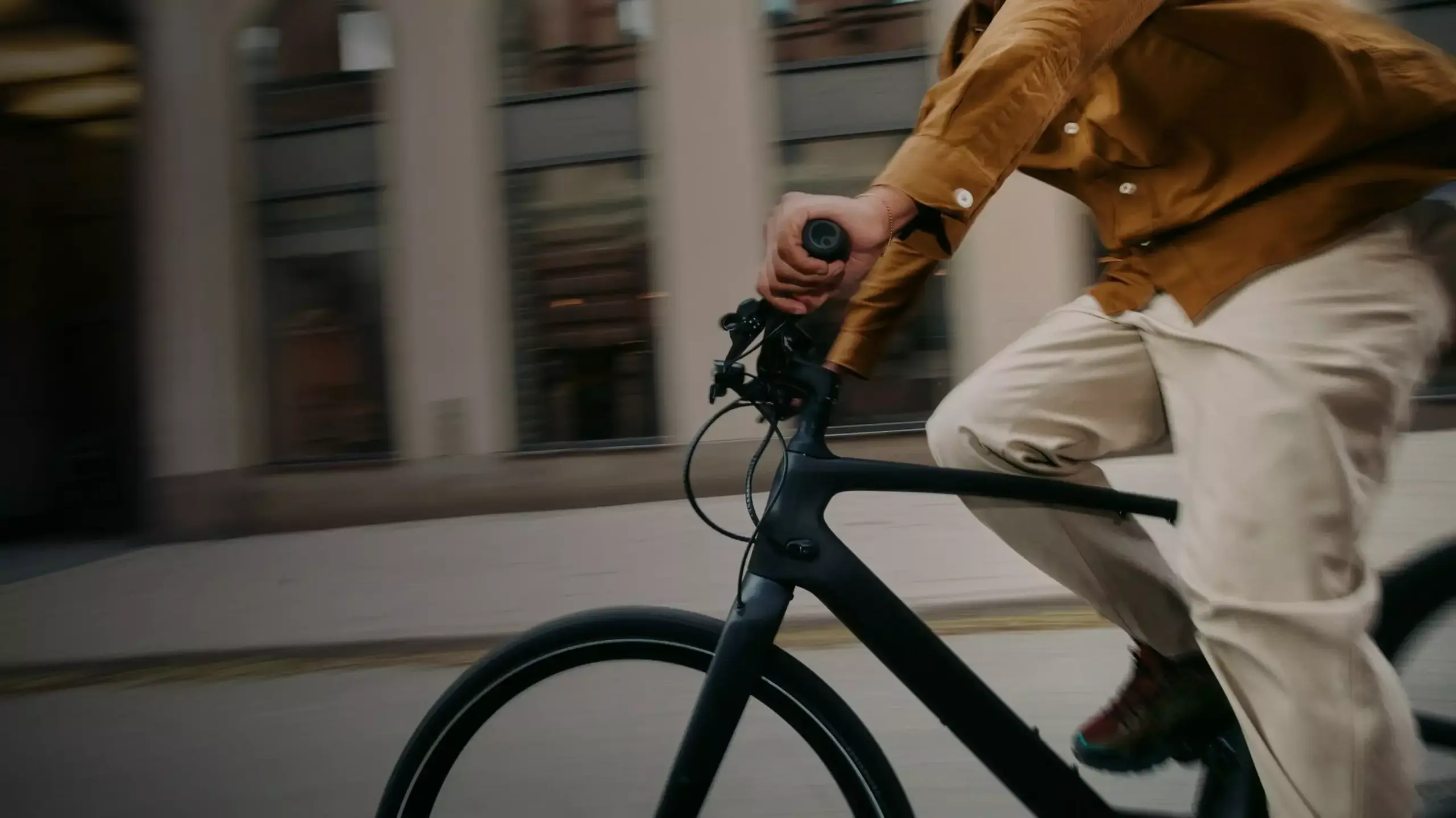 Fahrer mit senfgelbem Hemd und beiger Hose auf einem schwarzen Specialized Turbo Vado SL 2 5.0 EQ E-Bike mit Stadtkulisse im Hintergrund.