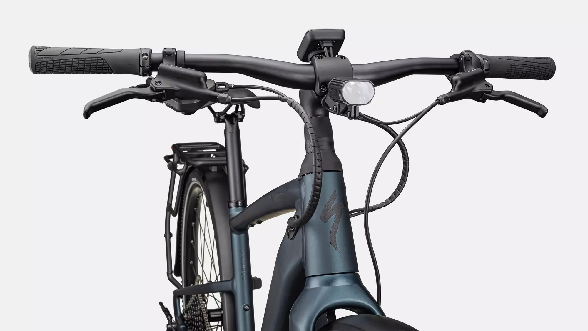 Vorderansicht eines Specialized Turbo Vado SL 2 5.0 EQ E-Bikes in Satin Deep Lake Metallic. Das Bild zeigt den Lenker mit ergonomischen Griffen, Bremshebeln, integriertem Display und Frontlicht. Der vordere Teil des Rahmens mit dem Specialized-Logo ist ebenfalls gut sichtbar.