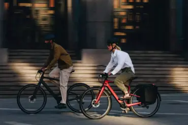 Zwei Personen, eine Frau und ein Mann, fahren E-Bikes nebeneinander auf einer Straße.