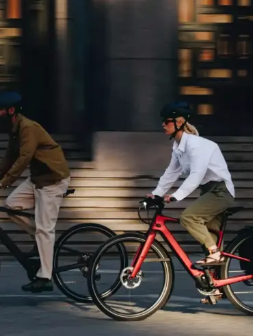 Zwei Personen, eine Frau und ein Mann, fahren E-Bikes nebeneinander auf einer Straße.
