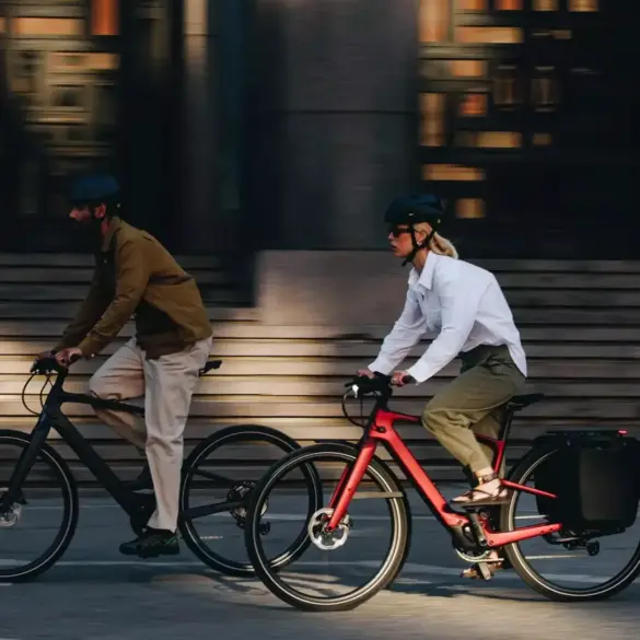 Zwei Personen, eine Frau und ein Mann, fahren E-Bikes nebeneinander auf einer Straße.