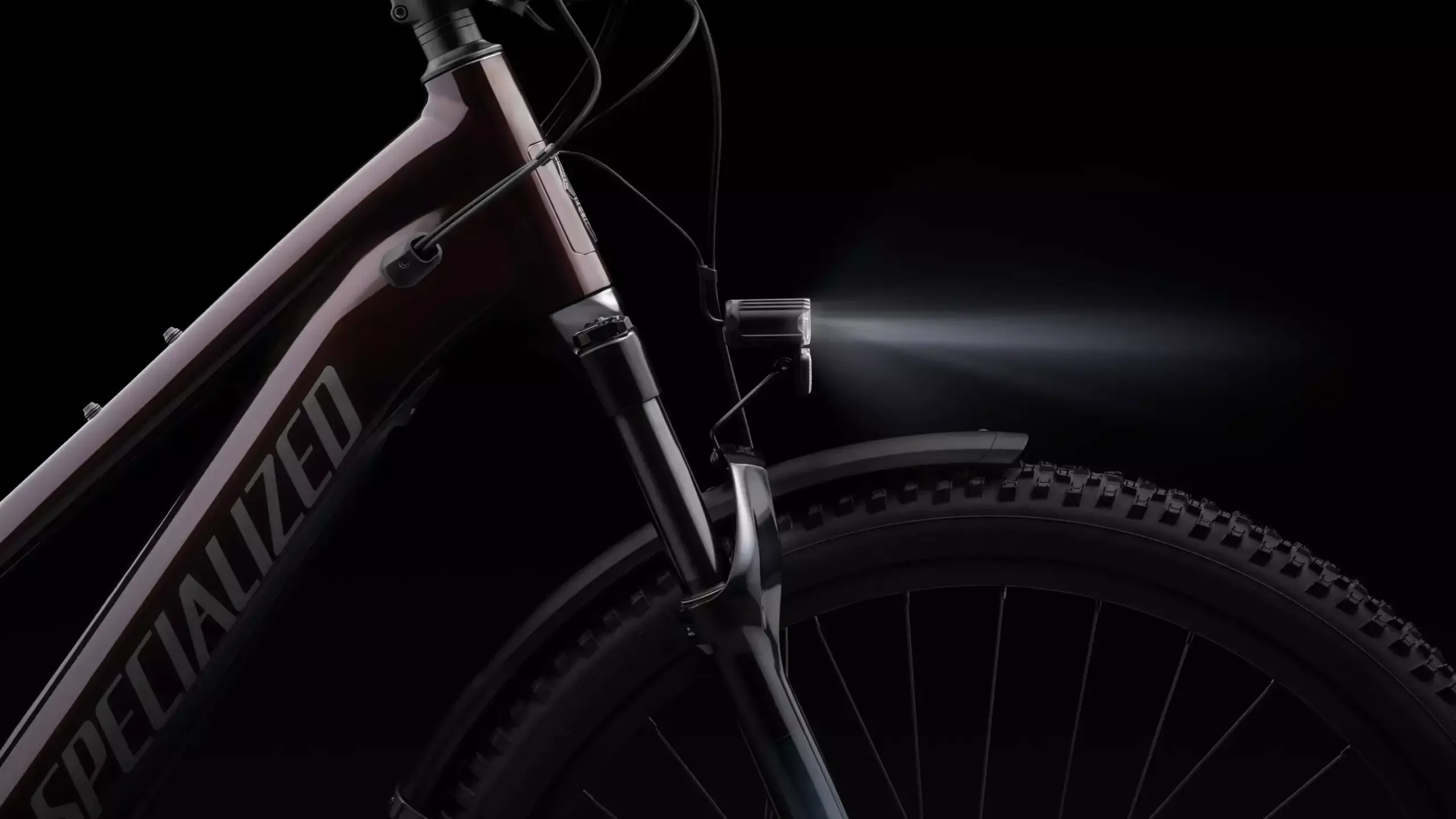Nahaufnahme des dunkelroten Rahmens eines Specialized Turbo Vado SL 2 6.0 EQ Carbon E-Bikes mit eingeschaltetem Frontlicht und sichtbarer Federgabel.