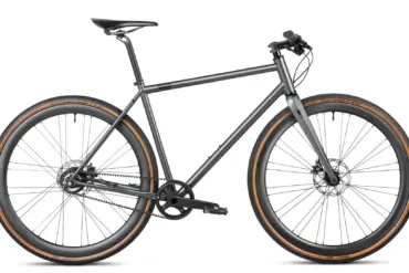 Seitenansicht eines stark grey Gravelbikes mit Stahlrahmen, Flatbar-Lenker, Gates Carbon Drive Riemenantrieb und Continental Terra Speed Reifen.