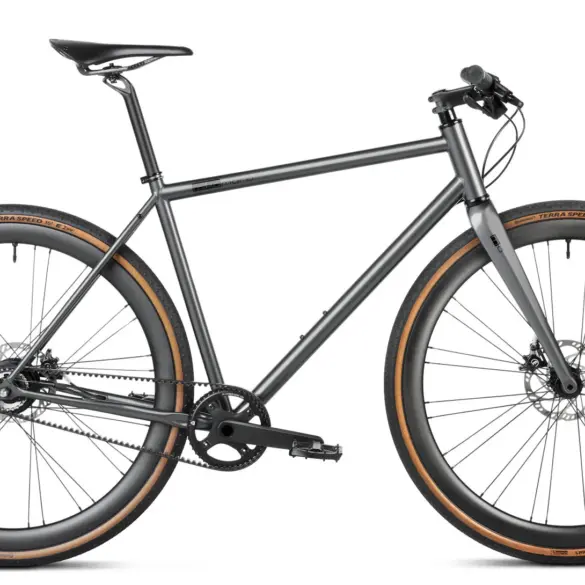 Seitenansicht eines stark grey Gravelbikes mit Stahlrahmen, Flatbar-Lenker, Gates Carbon Drive Riemenantrieb und Continental Terra Speed Reifen.