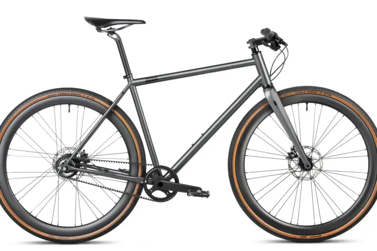 Seitenansicht eines stark grey Gravelbikes mit Stahlrahmen, Flatbar-Lenker, Gates Carbon Drive Riemenantrieb und Continental Terra Speed Reifen.